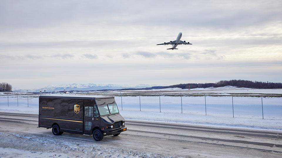 A UPS truck driving in snow as an airplane takes off